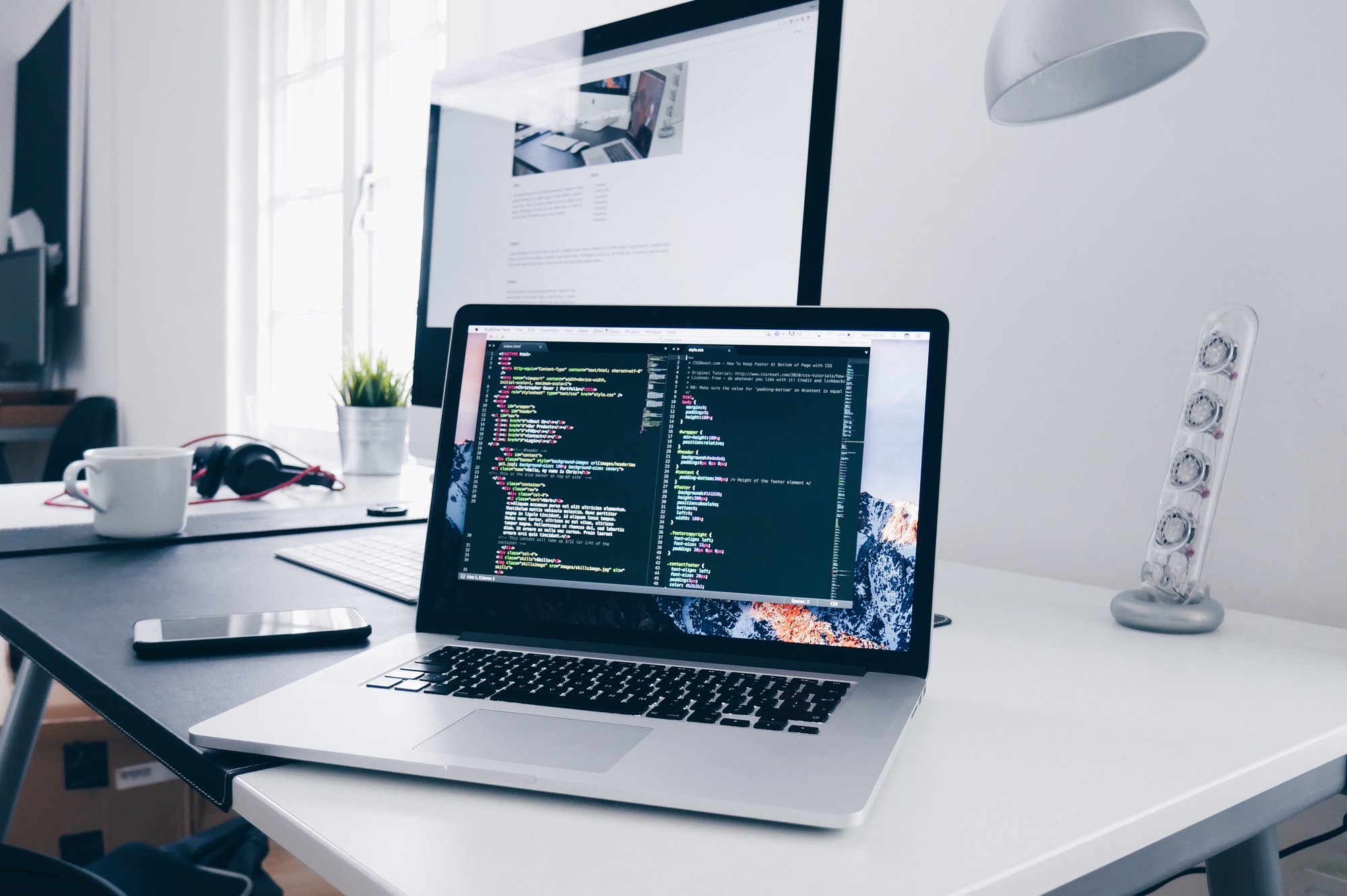 An open MacBook on top of a silver desk with code on its screen.