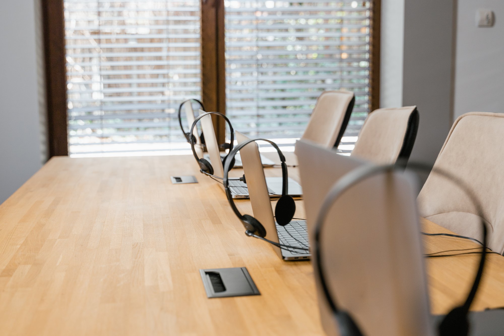 A conference call meeting room with a wooden table and multiple laptops and headsets on top of it.